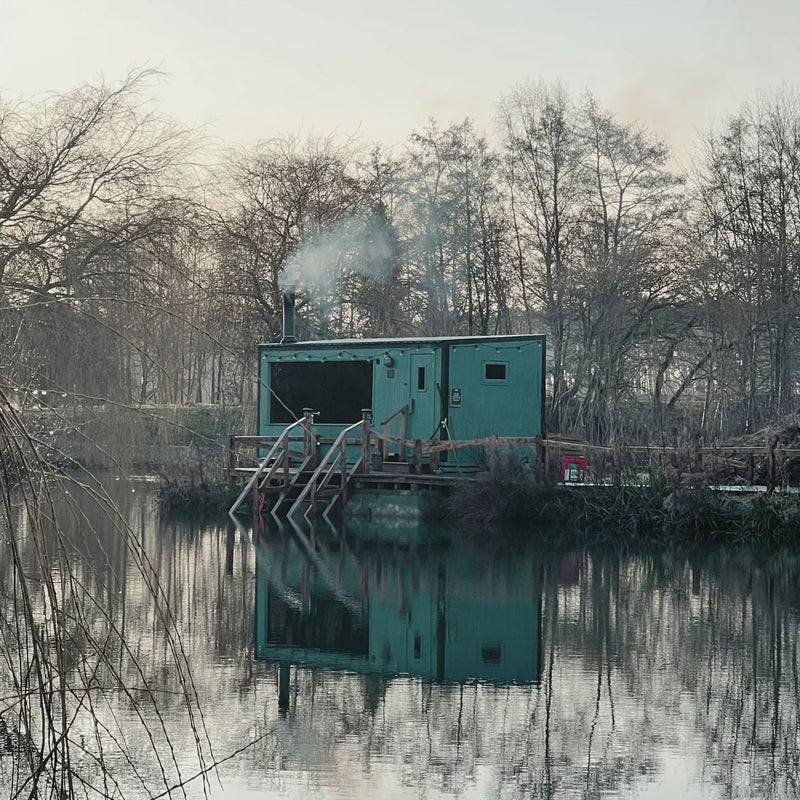 Wood-fired lakeside sauna reflected in still winter water before a cold-water swim